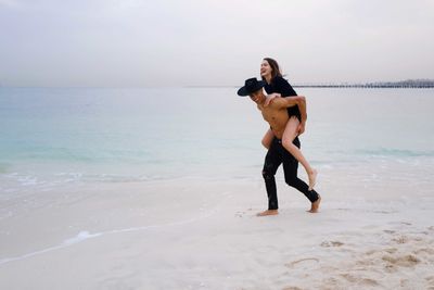 Full length of young couple having fun doing piggyback ride at the beach