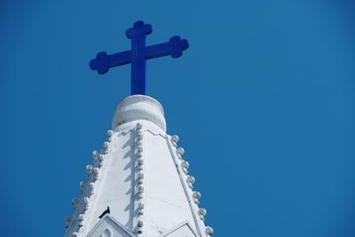 Low angle view of cross amidst buildings against clear blue sky