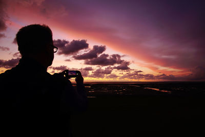 Silhouette man photographing against sky during sunset