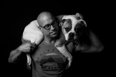 Portrait of shirtless man holding dog against black background