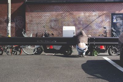 Rear view of man crouching on street by parking lot