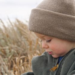 Close-up of long dark lashed toddler boy  looking down in field in winter clothing