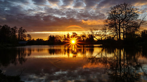 Silhouette trees by lake against sky during sunset