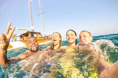 Portrait of cheerful friends swimming in sea against clear sky