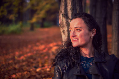 Portrait of smiling woman standing on tree trunk