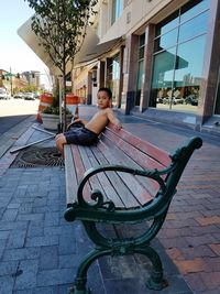 Portrait of woman sitting on footpath against building