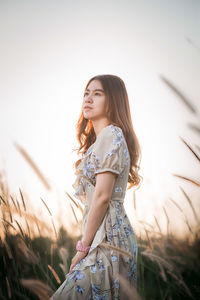 Thoughtful young woman standing against clear sky during sunset