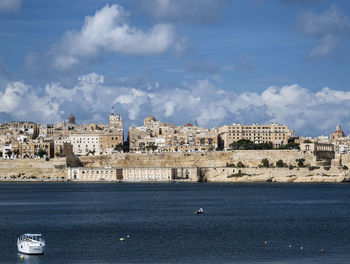 Buildings by sea against cloudy sky