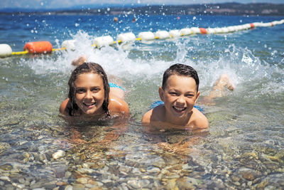 Portrait of smiling siblings swimming in sea on sunny day