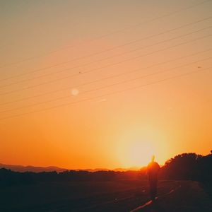 Silhouette man standing on mountain against orange sky