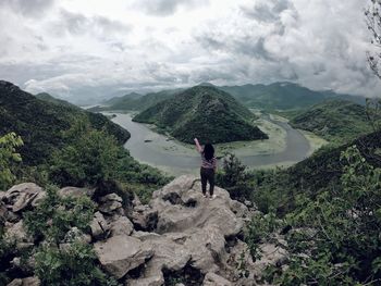 Woman sitting on rock against river and mountains