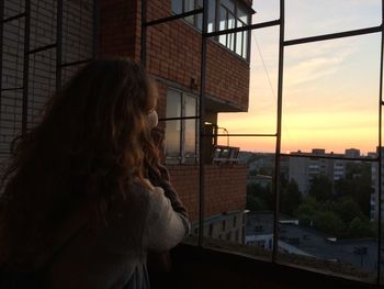 Woman looking through window during sunset