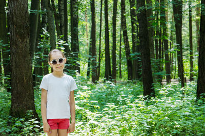 Man wearing sunglasses standing by tree trunk in forest