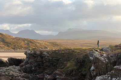 Woman standing on rock by mountains against sky