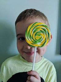 Portrait of smiling boy holding lollipop against wall