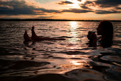 A young woman drinking tea and sitting in a lake at sunset 