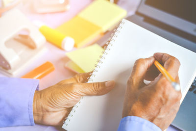 Cropped hands of businessman writing on notepad at desk