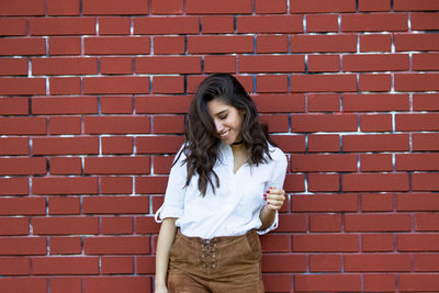 Beautiful young woman standing against brick wall