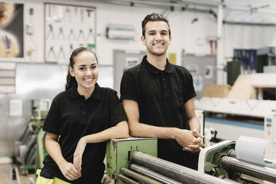 Portrait of smiling young high school students standing by machinery in workshop