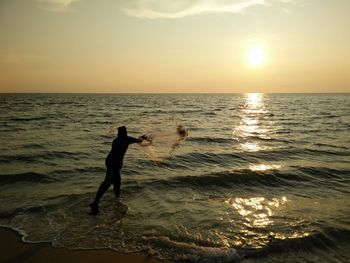 Silhouette man standing on beach against sky during sunset