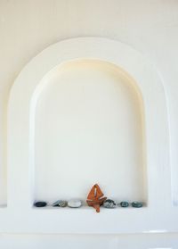 Pebbles and model boat in niche amidst white wall