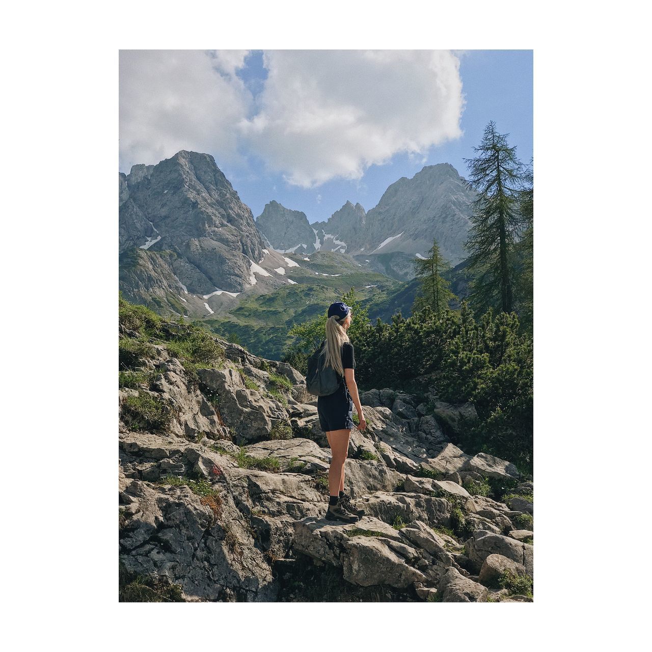 WOMAN STANDING ON ROCK AGAINST MOUNTAIN RANGE