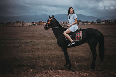 Woman and horse on field against cloudy sky