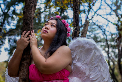 Young woman in angel costume holding tree trunk