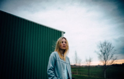 Thoughtful young woman looking away while standing against sky during sunset