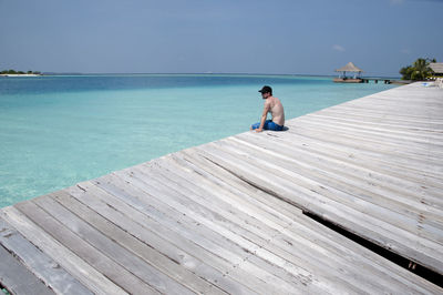 Shirtless man sitting in pier against sea