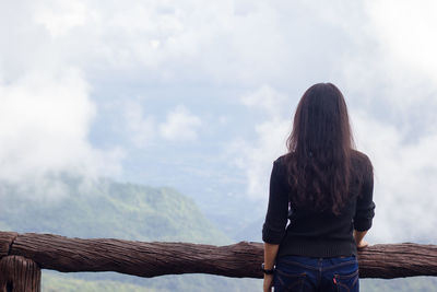 Rear view of woman looking at mountain against cloudy sky