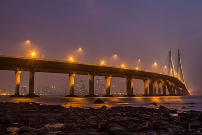 Illuminated bridge over sea against sky at night