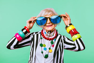 Portrait of senior woman wearing sunglasses against colored background