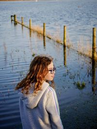 Girl looking away while standing by lake