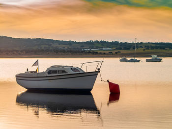 Boat moored on lake against sky during sunset