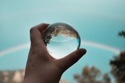 Close-up of hand holding crystal ball against sky