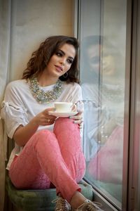 Young woman looking through window at home