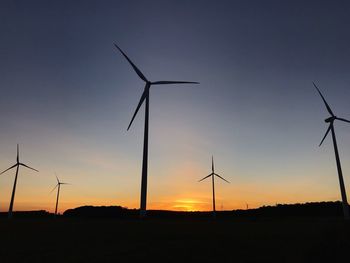 Silhouette wind turbines on field against sky during sunset