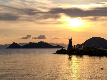 Silhouette built structure by sea against orange sky