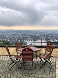 Empty chairs by river against buildings in city