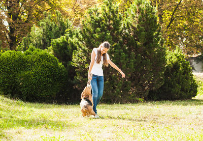 Full length of girl playing with dog against tree