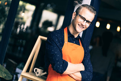 Portrait of male barista with arms crossed standing at cafe