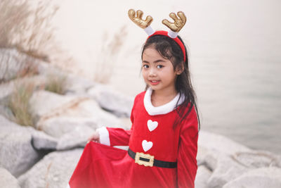 Portrait of cute girl wearing red dress and headband while standing at beach