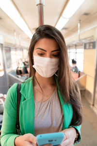 Young woman wearing mask using phone while sitting at subway train