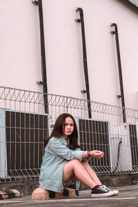 Portrait of young woman sitting against railing