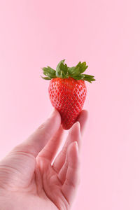 Midsection of person holding strawberry against pink background