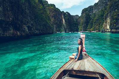 Woman sitting in boat in sea against mountains