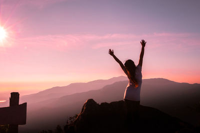 Rear view of woman with arms raised standing on mountain during sunset
