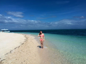 Full length of sensuous young woman in bikini standing at beach against sky