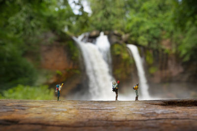 Hiking figurines on wood against waterfall in forest